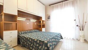Un dormitorio con cama, armario empotrado, mesitas de noche y ventana con cortinas.