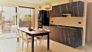 A modern kitchen with a dining area, a large window, and a view of greenery outside.