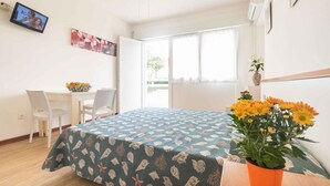 Een kamer met een bed, een bureau, stoelen, een televisie en een raam.