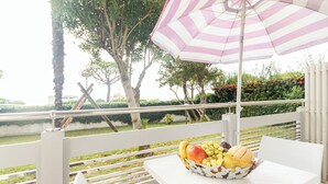 Een witte tafel met een fruitschaal en een gestreepte parasol op een terras.