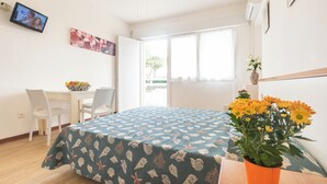 A room with a bed, a desk, chairs, a TV, and a window. - Studio with air conditioning (Lignano)