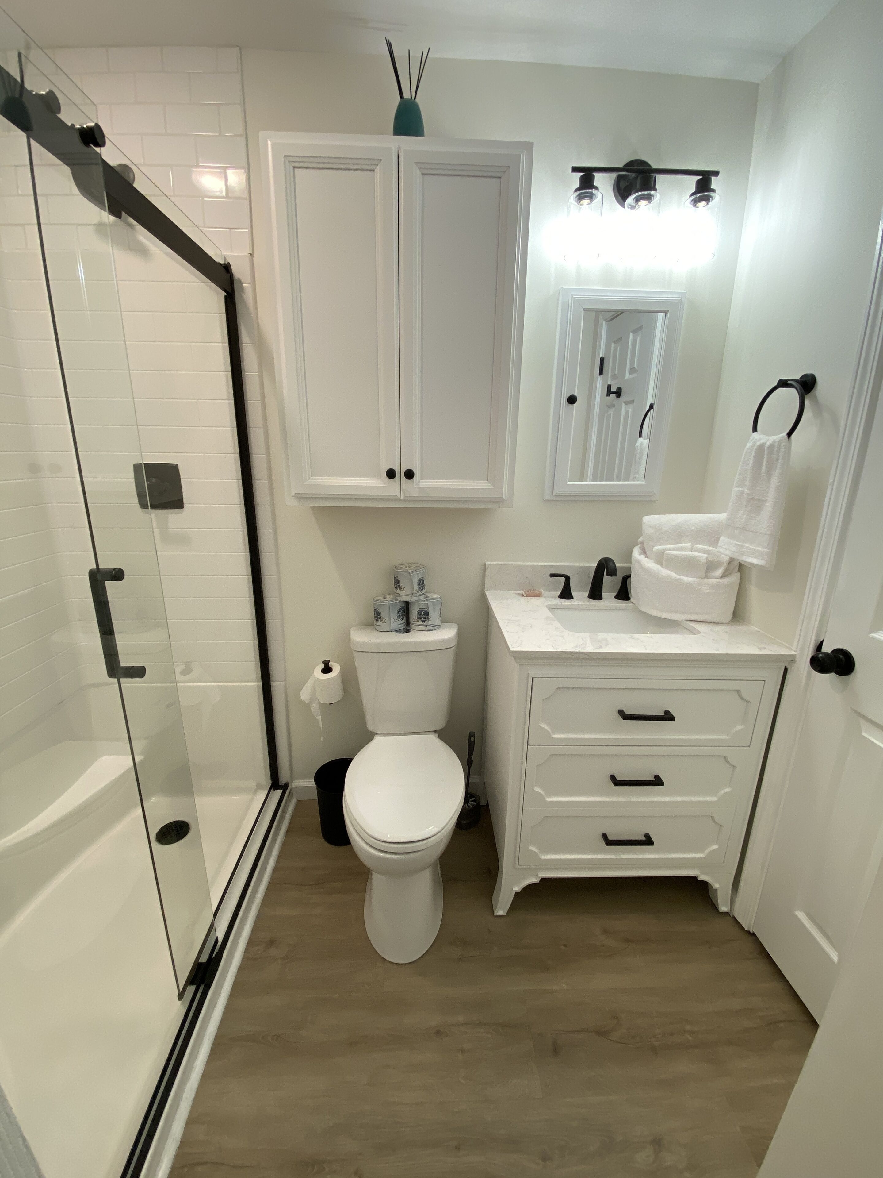 Een badkamer met een douchecabine van glas, een toilet, een wastafel met spiegel en een handdoekrek.