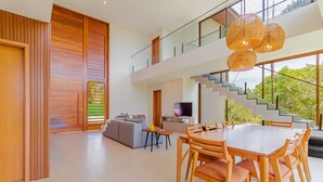 A modern interior with a dining area, a sofa, and a staircase. - PF47 High Standard House 5 Suites - Praia do Forte (Mata de São João)