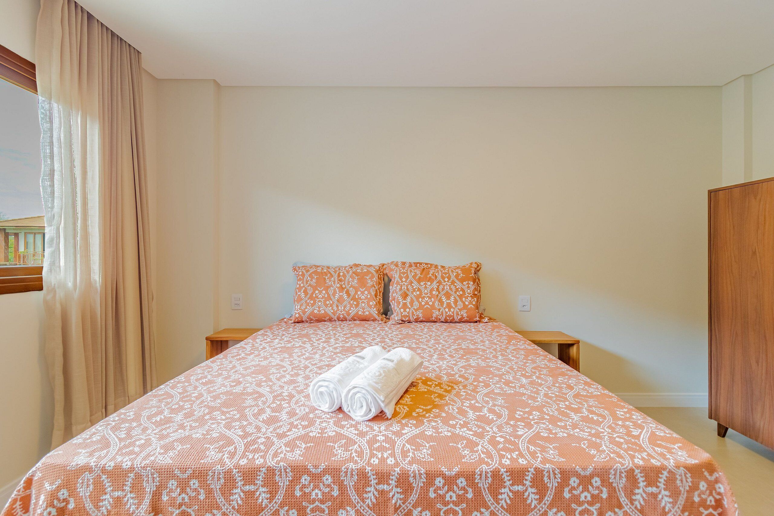 A neatly made bed with a patterned bedspread, two pillows, and rolled towels.