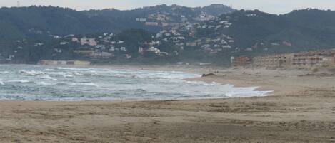 A beach with waves, a sandy shore, and buildings in the background.