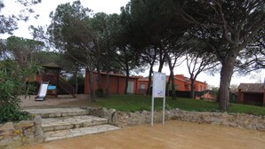 A courtyard with a stone floor, a playground, and a building with a red roof.
