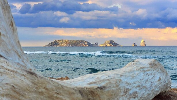 A large, smooth rock in the foreground with a view of the sea and rocky islands in the background.