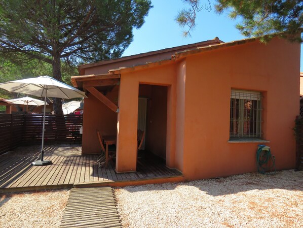 A small orange building with a wooden deck, a covered seating area, and a window with bars.