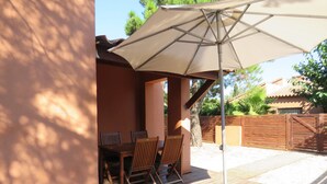 An outdoor patio with a wooden table and chairs, a large umbrella, and a wooden deck.