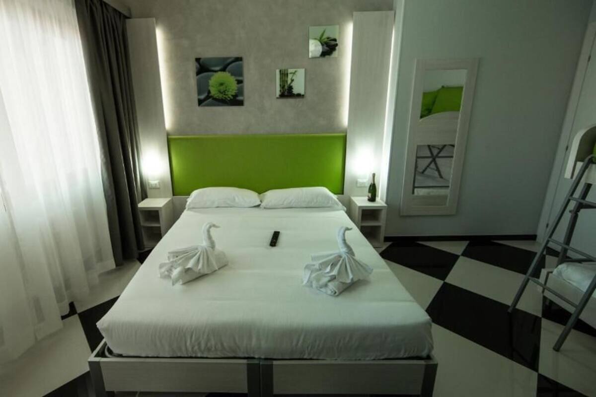 A hotel room with a bed, two white towels, a green headboard, a checkered floor, and artwork on the walls.