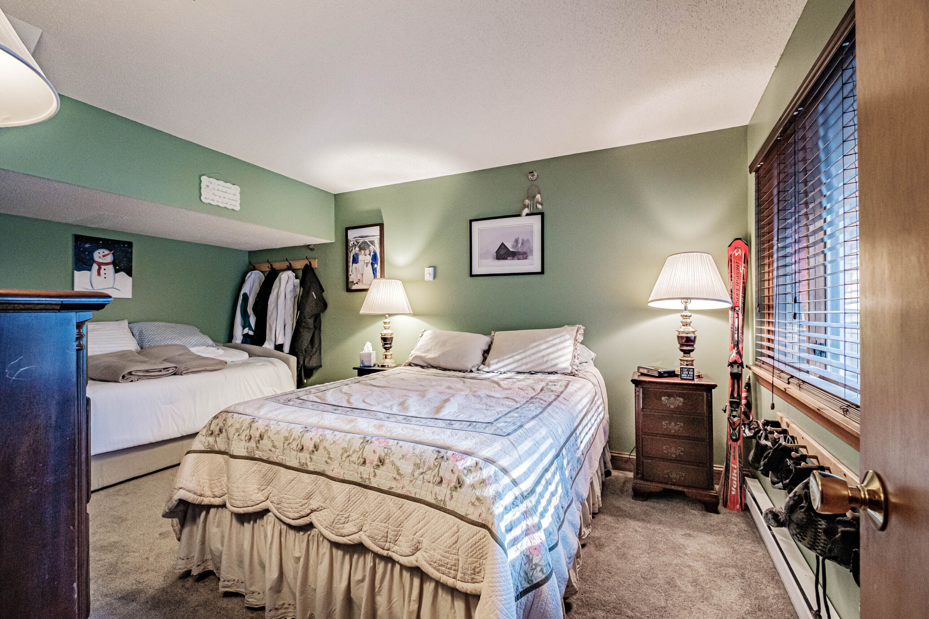 A bedroom with a large bed, two bedside tables, a dresser, and a window with blinds.