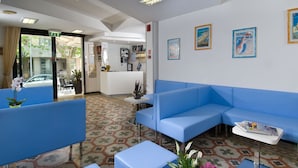 A reception area with blue seating, a patterned floor, and framed pictures on the wall. - Hotel Mirabella (Cattolica)