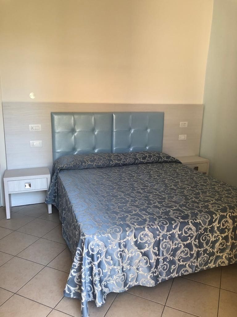 Een slaapkamer met een gestuukt hoofdeinde, een bed met een decoratieve sprei, een nachtkastje en een bijzettafeltje.