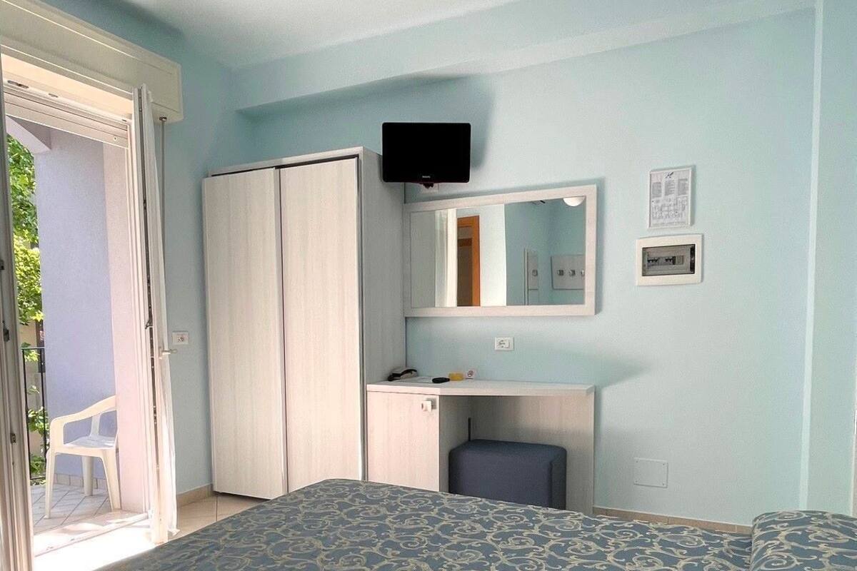 A bedroom with a bed, a desk, a chair, a wardrobe, a ceiling fan, and a television.