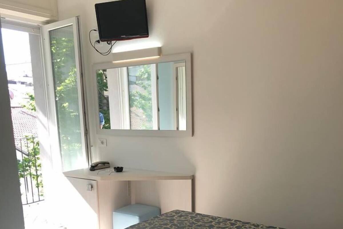 A room with a bed, a desk, a chair, a television mounted on the wall, and a window.