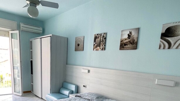 A bedroom with a bed, a nightstand, a wardrobe, and a ceiling fan. - Hotel Mirabella (Cattolica)