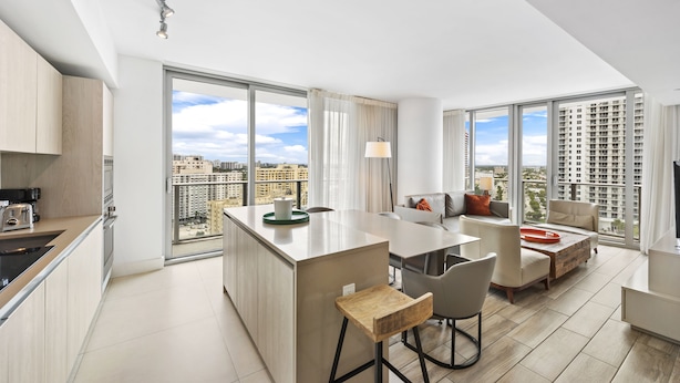 Um apartamento moderno com cozinha, área de refeições e sala de estar. Possui grandes janelas com vista para a cidade.