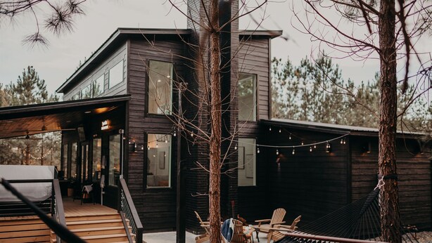 Una casa moderna de madera con un porche cubierto, asientos exteriores y una hamaca.
