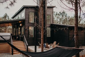 Et moderne træhus med overdækket veranda, udendørs møbler og en hængekøje.