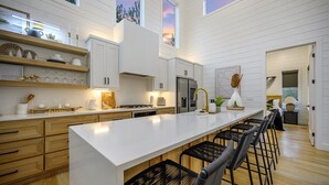 Una cocina moderna con armarios blancos, una isla grande con taburetes y vistas al atardecer a través de las ventanas.