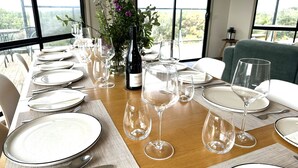 A dining table set for a meal with plates, cutlery, and wine glasses, with a vase of flowers and a bottle of wine in the center. - Beachfront at Cape Paterson (Cape Paterson)