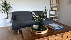 A modern living room with a grey sofa, a wooden coffee table with a vase and books, a potted plant, and a bookshelf in the background. - Beachfront at Cape Paterson (Cape Paterson)
