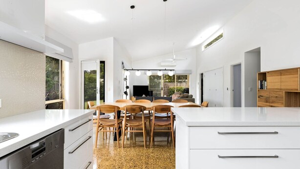 A modern kitchen with white cabinetry, a central island with stools, and a dining area with a TV.