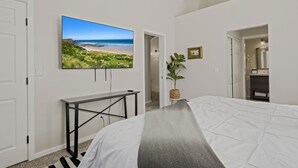 A bedroom with a bed, a TV on the wall, a desk, and a plant.