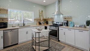 A modern kitchen with white cabinets, a stainless steel dishwasher, a gas stove, and a large window with blinds.