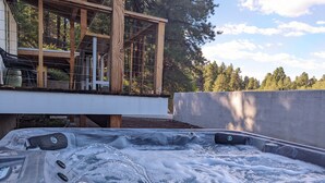 A hot tub with a wooden deck and a view of trees.