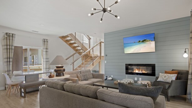 A modern living room with a fireplace, a large TV, and a staircase leading to another level.