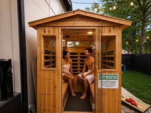A sauna with two people inside, a safety instruction sign, and a wooden exterior.