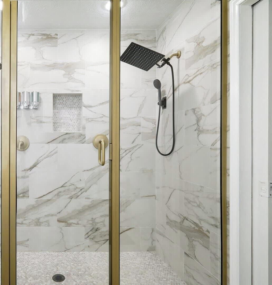 Eine Dusche ohne trittfeste Einstieg, mit Glasabtrennung, Marmorwänden und einer Handbrause.