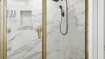 Eine Dusche ohne trittfeste Einstieg, mit Glasabtrennung, Marmorwänden und einer Handbrause.