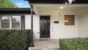 A modern house with a black door, a welcome sign, and a small window on the right. - Panoramic 4BR/3B Home with Pool, Grill, Sauna & Game Room (Dallas)