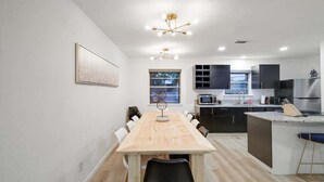 A modern kitchen with a wooden dining table, black chairs, and a built-in island with a sink. - Panoramic 4BR/3B Home with Pool, Grill, Sauna & Game Room (Dallas)