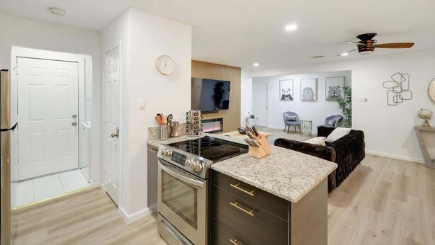 A modern kitchen with a built-in oven and stove, a dining area with a dark-colored sofa, and a ceiling fan. - Panoramic 4BR/3B Home with Pool, Grill, Sauna & Game Room (Dallas)