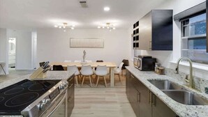 A modern kitchen with a central island, built-in appliances, and a dining area with a large table and chairs. - Panoramic 4BR/3B Home with Pool, Grill, Sauna & Game Room (Dallas)