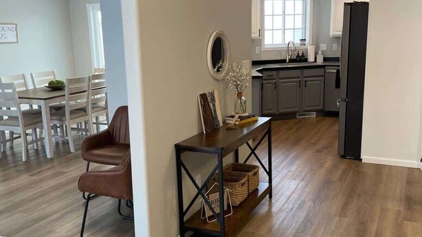 Amplia sala de estar con piso de madera, zona de comedor con mesa y sillas, y cocina con armarios y un refrigerador.
