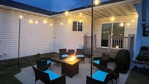 Un área de patio al aire libre con un pozo de fuego, asientos e iluminación colgante.
