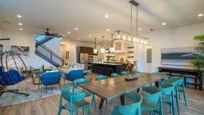 Un salón moderno con una mesa de comedor de madera, sillas azul verdosas, un sofá azul y una lámpara colgante.
