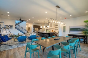 Un salón moderno con una mesa de comedor de madera, sillas azul verdosas, un sofá azul y una lámpara colgante.