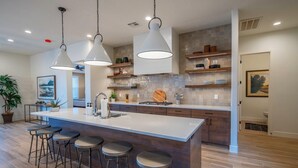 Una cocina moderna con una isla grande, taburetes de bar, iluminación colgante y estantes de madera.