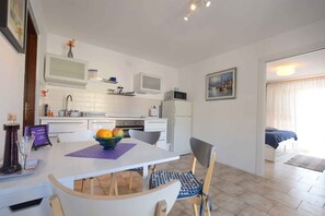 A modern kitchen with white cabinets, a dining table with chairs, a fruit bowl, and a painting on the wall. - Holiday apartment with beautiful sea views (Omišalj)