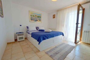 A bedroom with a bed, a nightstand, a painting, a window with curtains, and a radiator.