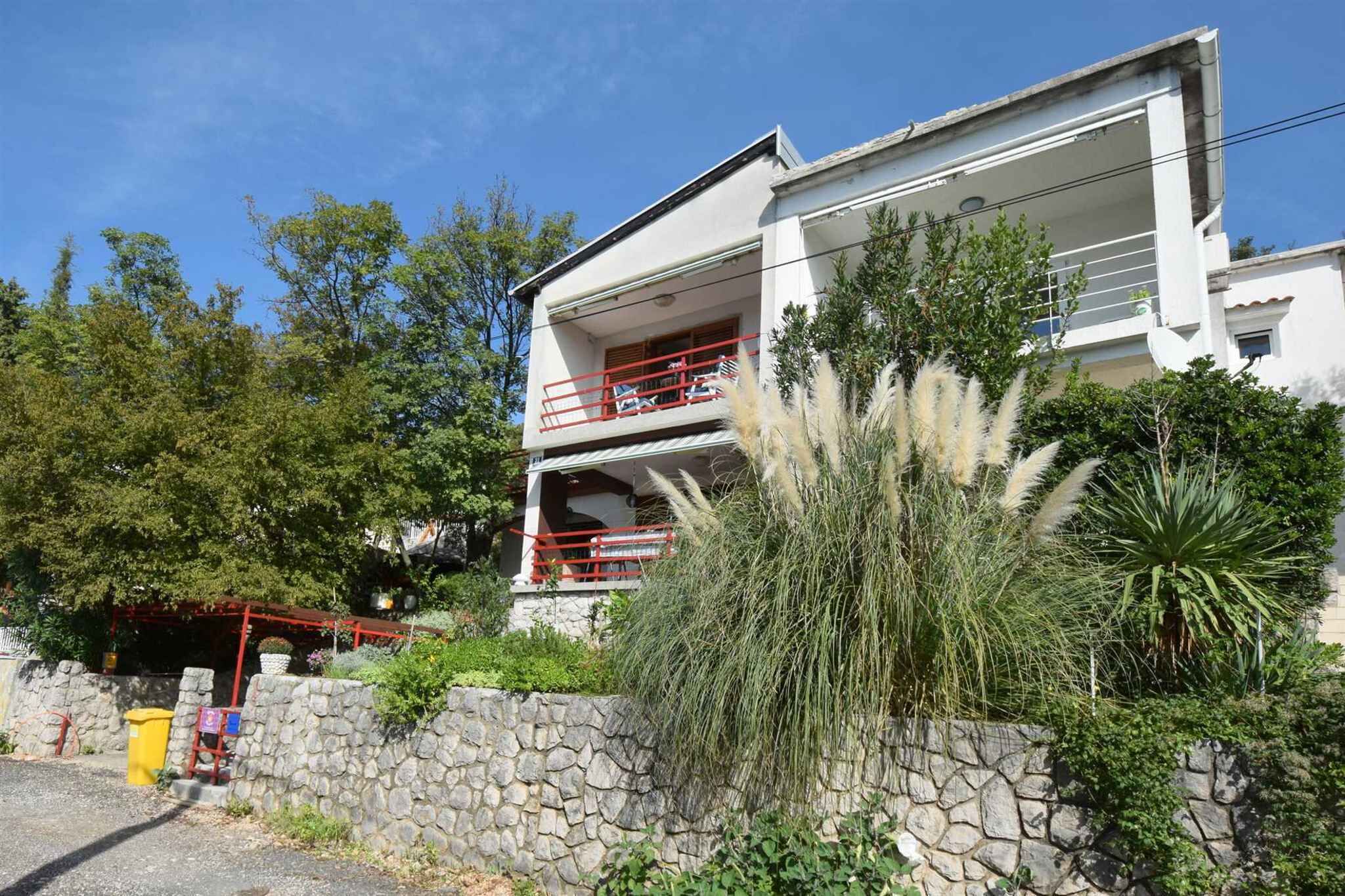A two-story building with balconies, surrounded by greenery and stone walls.