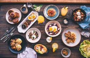 Une variété de plats pour le petit-déjeuner sont disposés sur une table en bois, notamment des œufs, du bacon et des toasts.