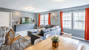 Una sala de estar moderna con un sofá gris, una mesa de comedor y un televisor montado en la pared.