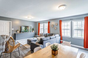 A modern living room with a grey sofa, a dining table, and a TV mounted on the wall.