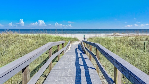 A wooden boardwalk leading to a beach with sand dunes and a clear blue sky.